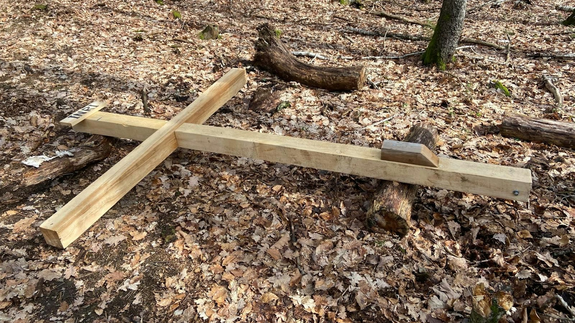 Ein großes Holzkreuz liegt auf einem Waldboden.