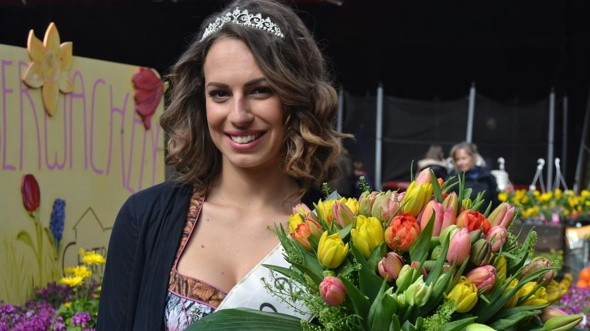 Das Foto zeigt eine Frau mit Schärpe, Krone und einem großen Strauß Tulpen.