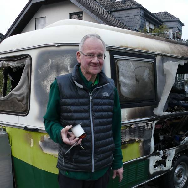 Ein Mann steht vor einem von Feuer völlig zestörten Wohnwagen.