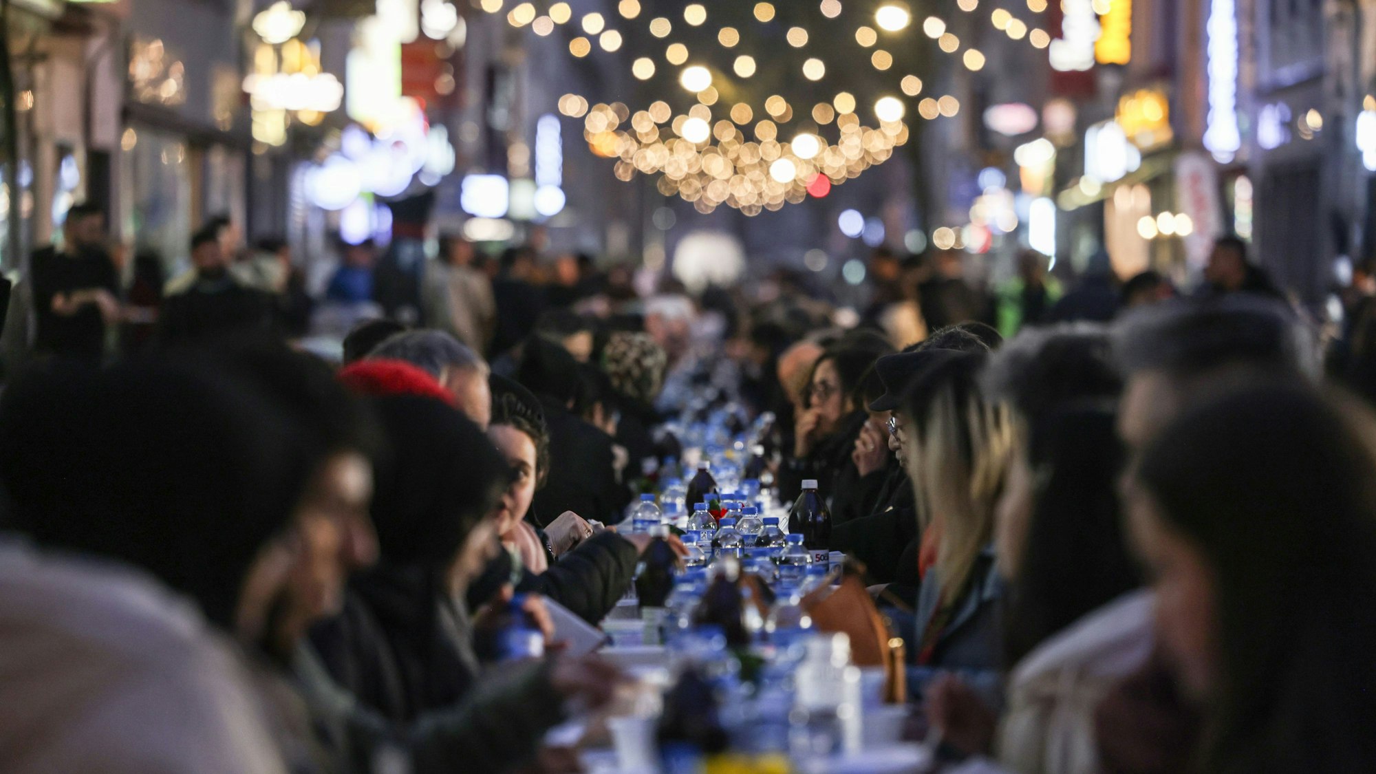 26.03.2025, Nordrhein-Westfalen, Köln: Zahlreiche Menschen sitzen zum Fastenbrechen in der Keupstraße an einem langen Tisch. Die Einzelhändler der Keupstraße haben zum gemeinsamen Fastenbrechen am Ende des Fastenmonats Ramadan eingeladen. Foto: Oliver Berg/dpa +++ dpa-Bildfunk +++