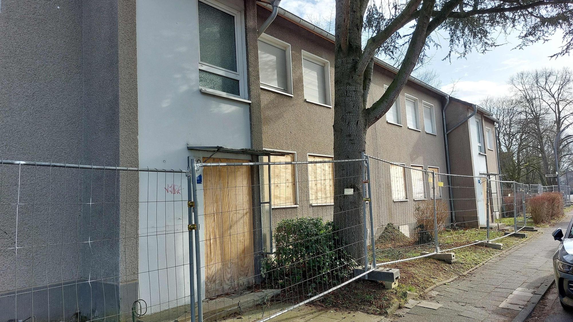 Häuser mit verrammelten Fenstern und Türen stehen hinter einem Bauzaun.