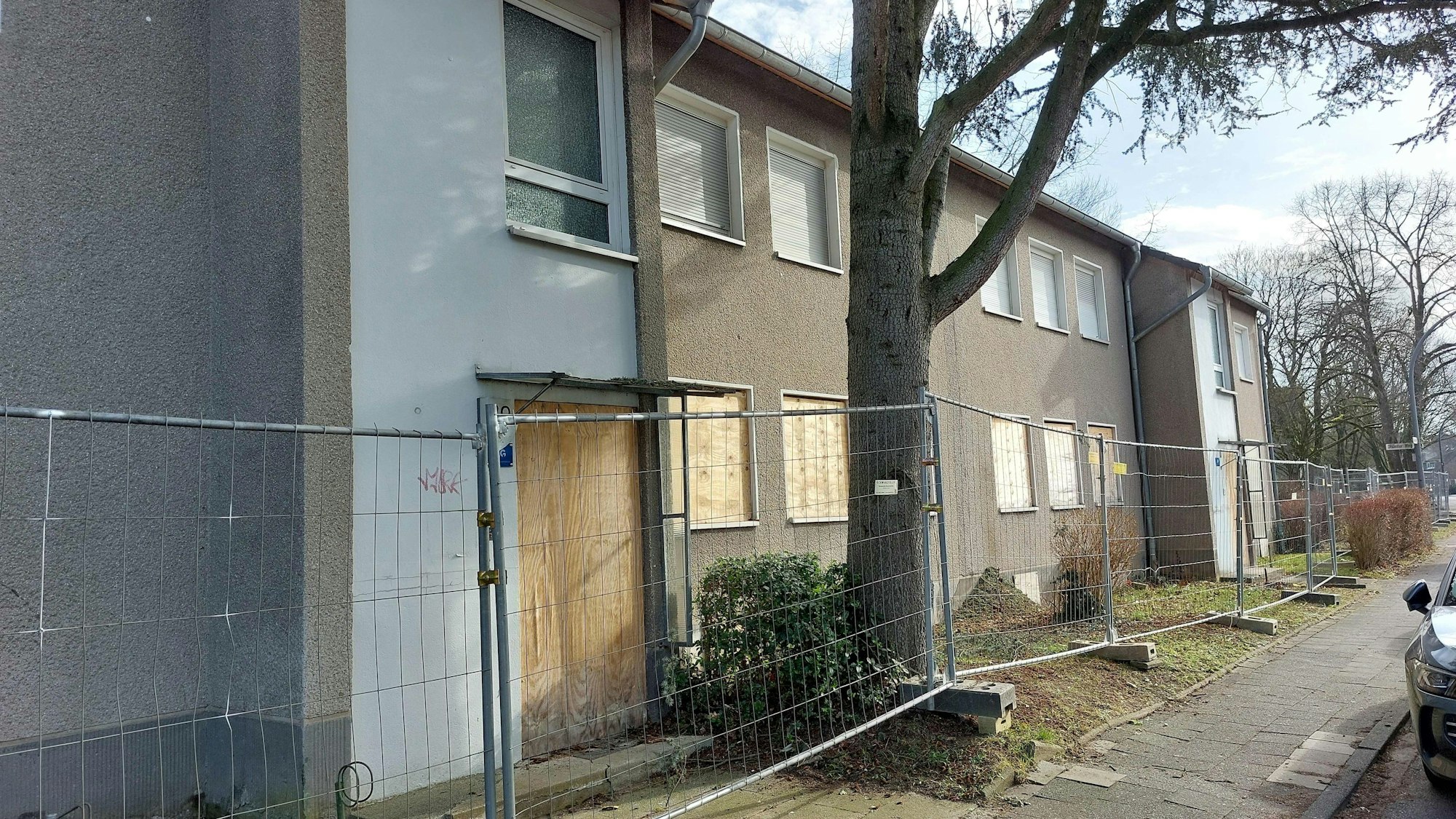 Häuser mit verrammelten Fenstern und Türen stehen hinter einem Bauzaun.