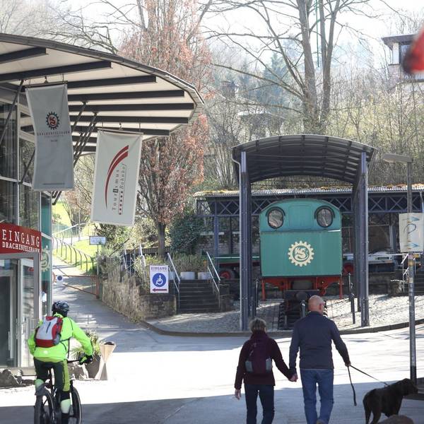 Die Glasfassade am Eingang der Drachenfelsbahn, im Hintergrund eine grüne Lok, die als Denkmal installiert ist.