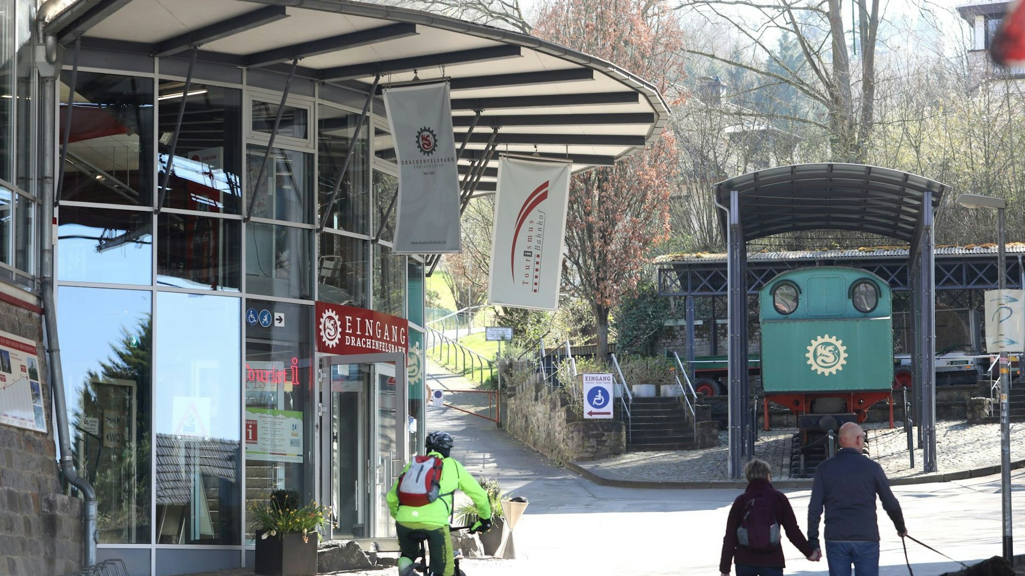 Die Glasfassade am Eingang der Drachenfelsbahn, im Hintergrund eine grüne Lok, die als Denkmal installiert ist.