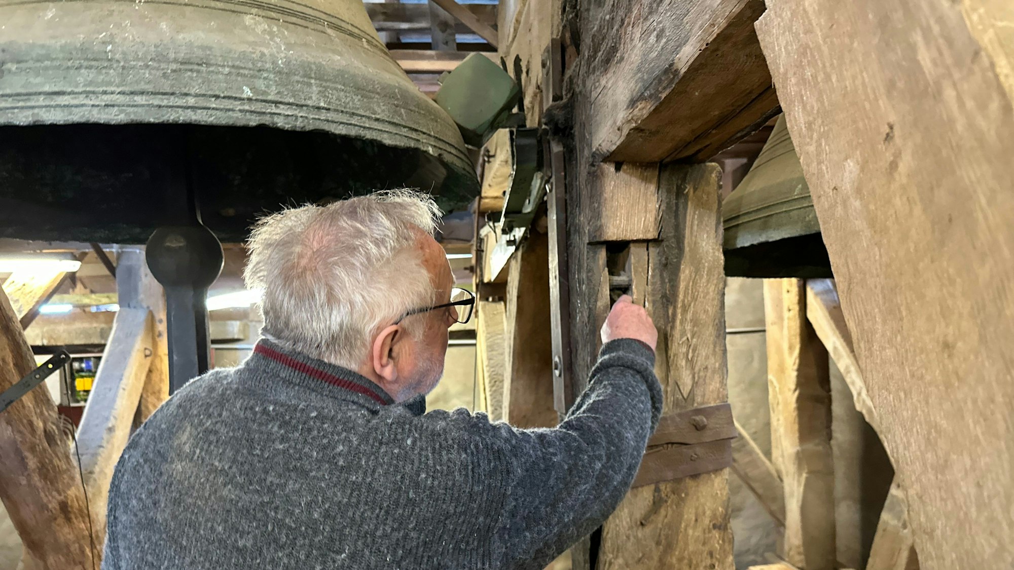 Manfred Bethge an der Glocke Anna. Er zeigt auf einen alten Eichenbalken, der vorher in einem Fachwerkhaus verwendet wurde. Zu erkennen sei dies an der rechteckigen Aussparung.