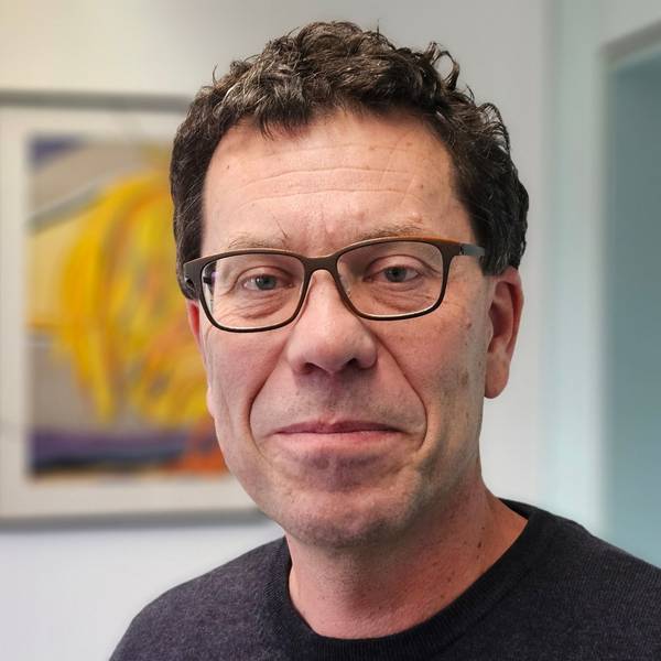 Auf dem Foto ist ein Mann mit Brille zu sehen. Er trägt einen dunklen Pullover.