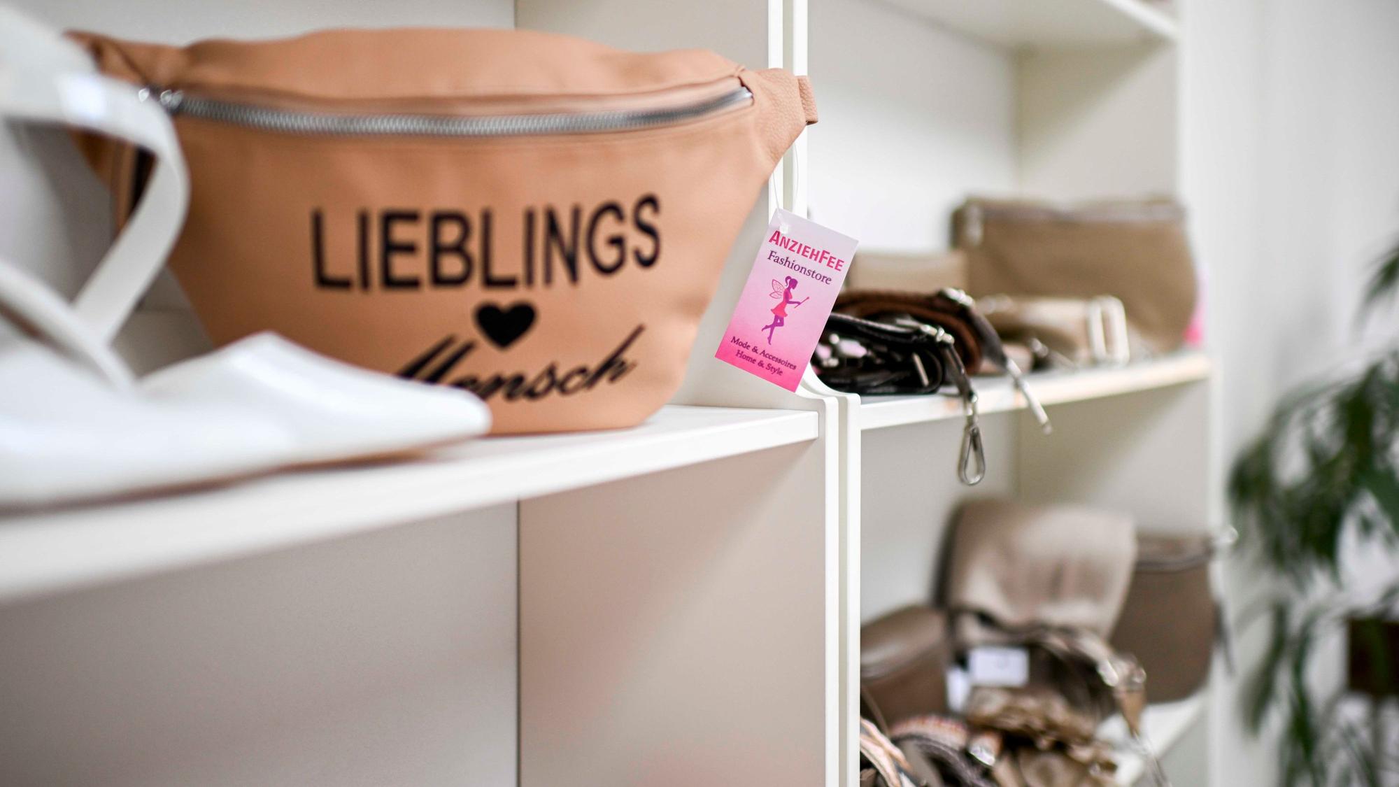 In einem weißen Regal des Modegeschäftes werden unterschiedliche Taschen zum Kauf angeboten.