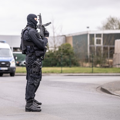 Zwei Polizeibeamte stehen an einer Straßensperre vor dem Platz in einem Industriegebiet in Burgsteinfurt, wo gerade eine Razzia läuft.