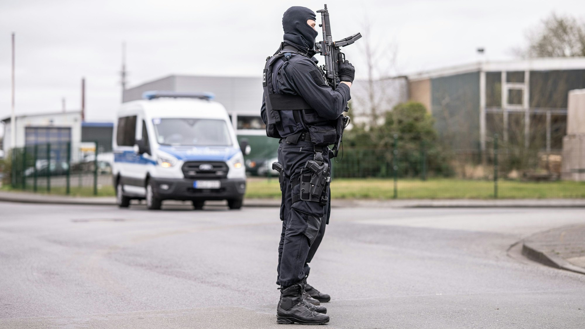 Zwei Polizeibeamte stehen an einer Straßensperre vor dem Platz in einem Industriegebiet in Burgsteinfurt, wo gerade eine Razzia läuft.