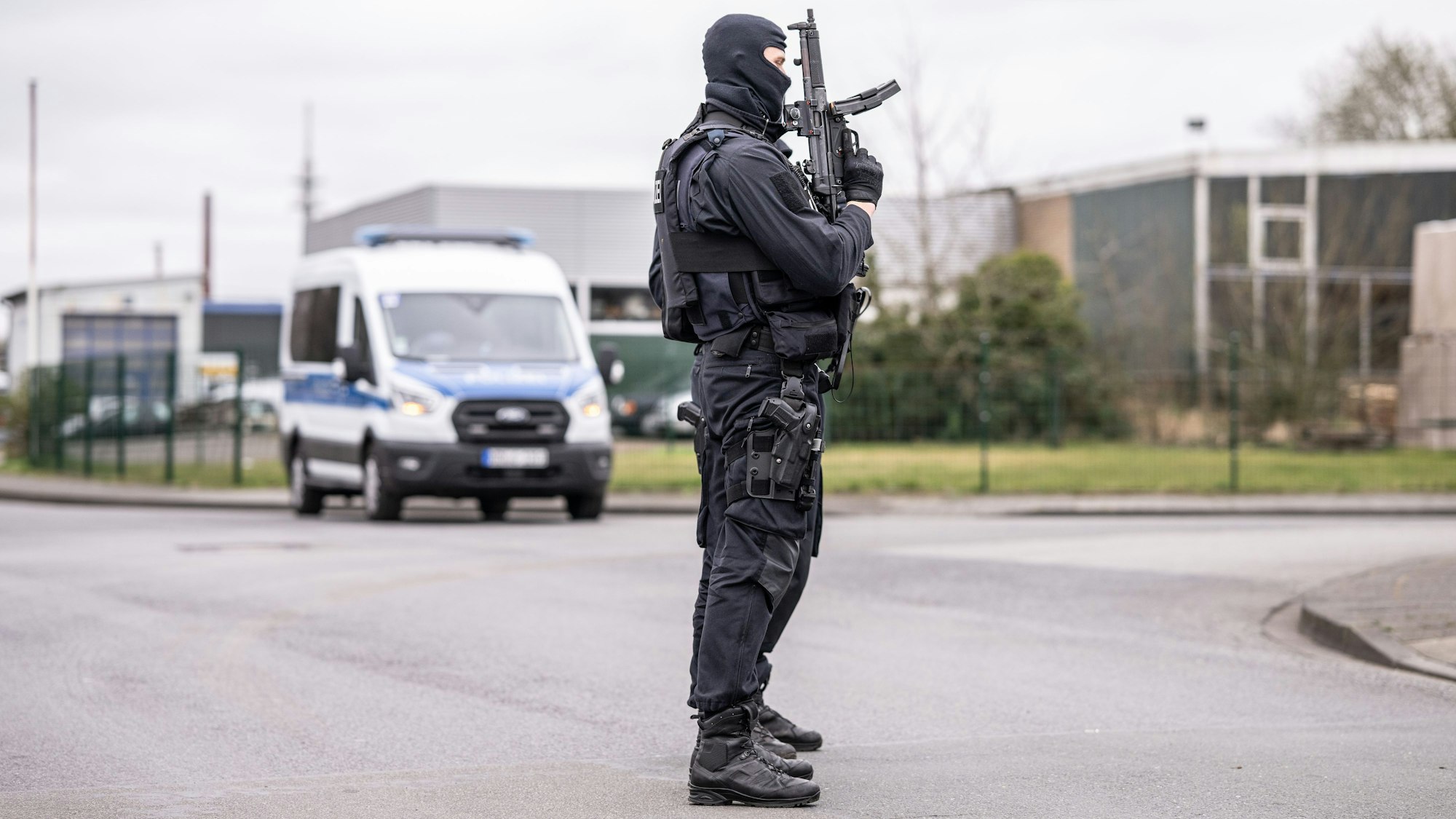 Zwei Polizeibeamte stehen an einer Straßensperre vor dem Platz in einem Industriegebiet in Burgsteinfurt, wo gerade eine Razzia läuft.