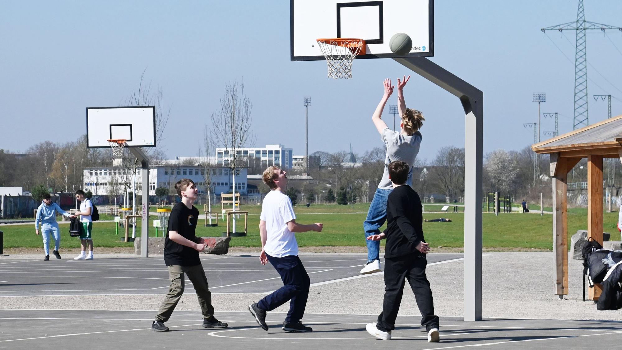 Zu sehen sind vier junge Menschen, die Basketball spielen.