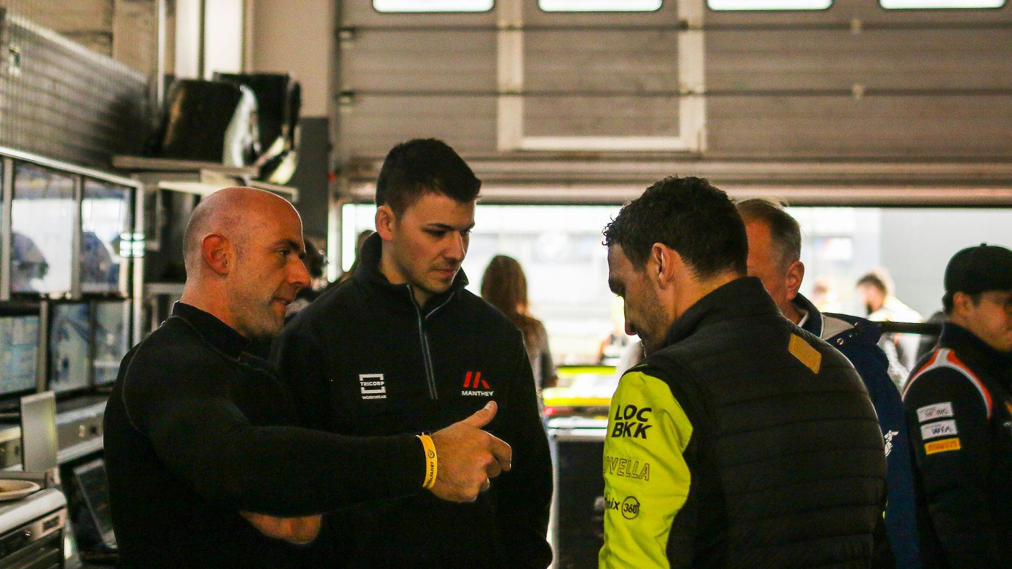 Drei Männer stehen in einer Box am Nürburgring und unterhalten sich.