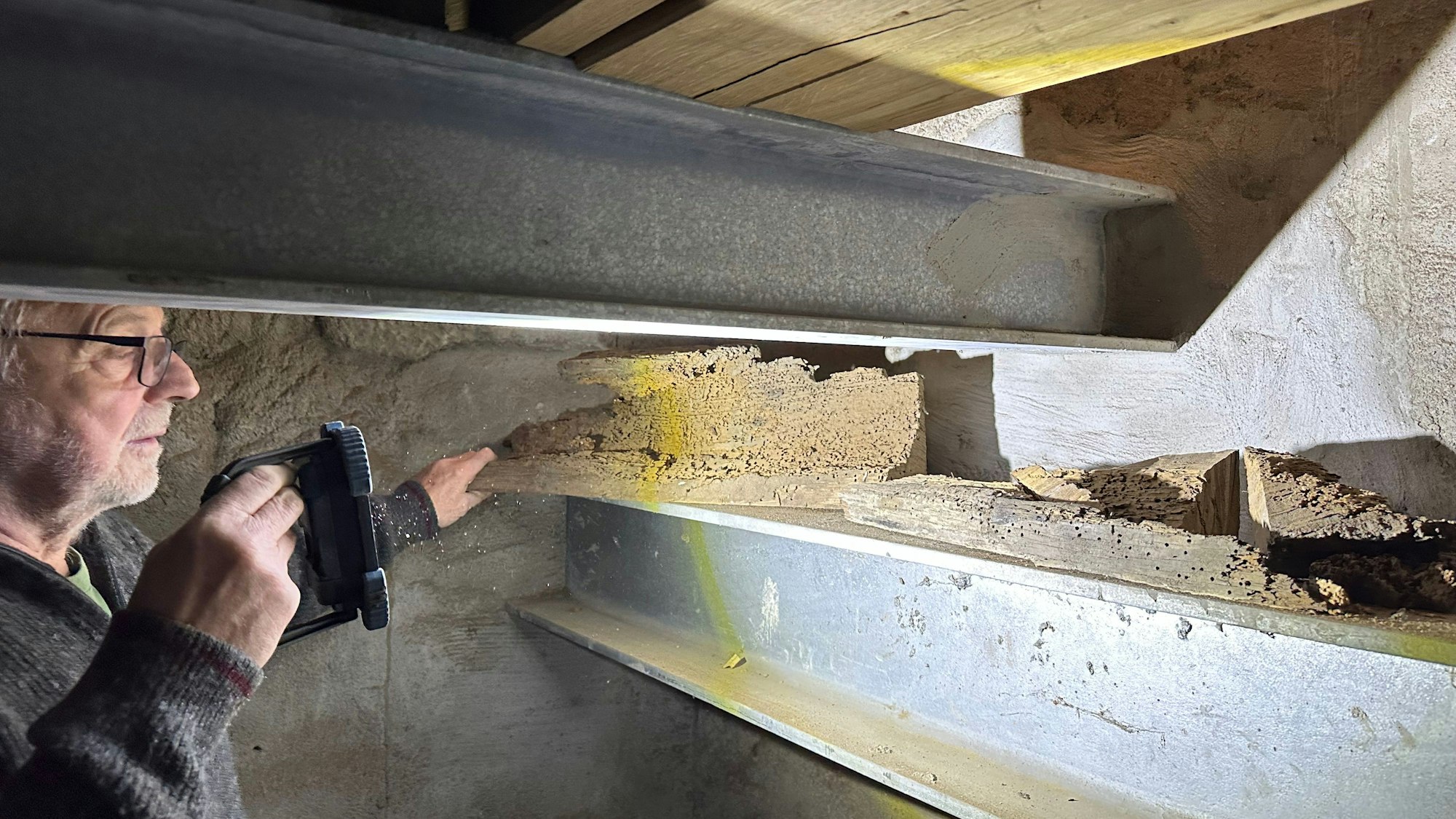 Ein Mann leuchtet mit der Taschenlampe auf eine Konstruktion aus Holz und Stahl.