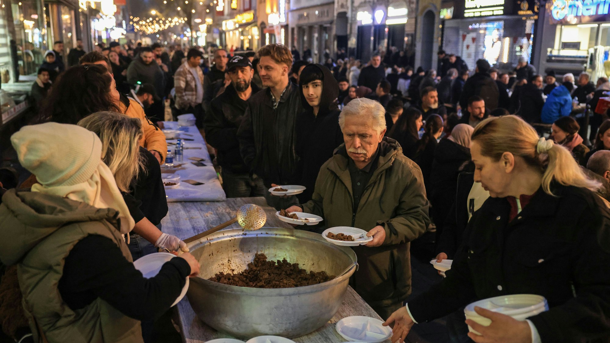 26.03.2025, Nordrhein-Westfalen, Köln: Menschen holen sich zum Fastenbrechen in der Keupstraße warmes Essen. Die Einzelhändler der Keupstraße haben zum gemeinsamen Fastenbrechen am Ende des Fastenmonats Ramadan eingeladen. Foto: Oliver Berg/dpa +++ dpa-Bildfunk +++