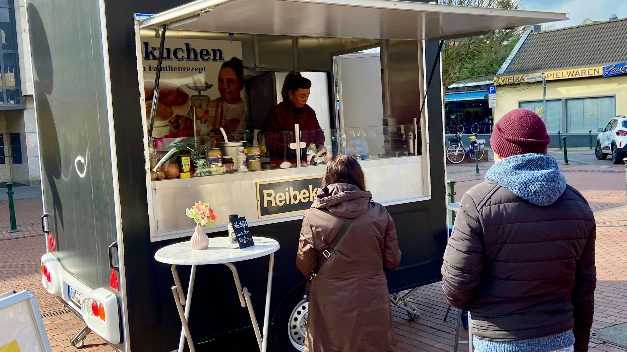 Ein Reibekuchenstand auf dem Wochenmarkt in Pulheim, davor stehen Kunden.