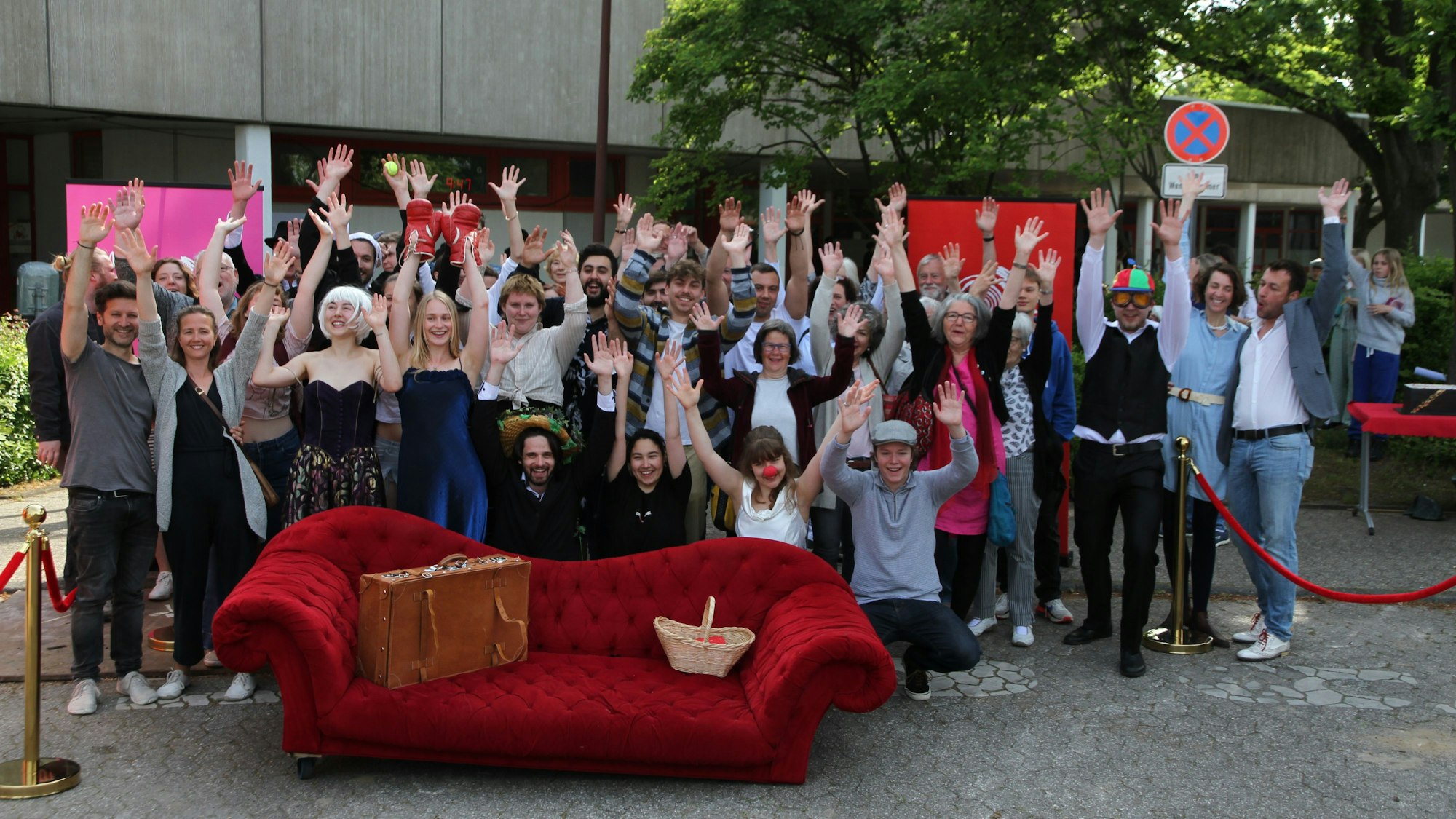 Eine Gruppe von jubelnden Schauspielern hinter einem roten Sofa.