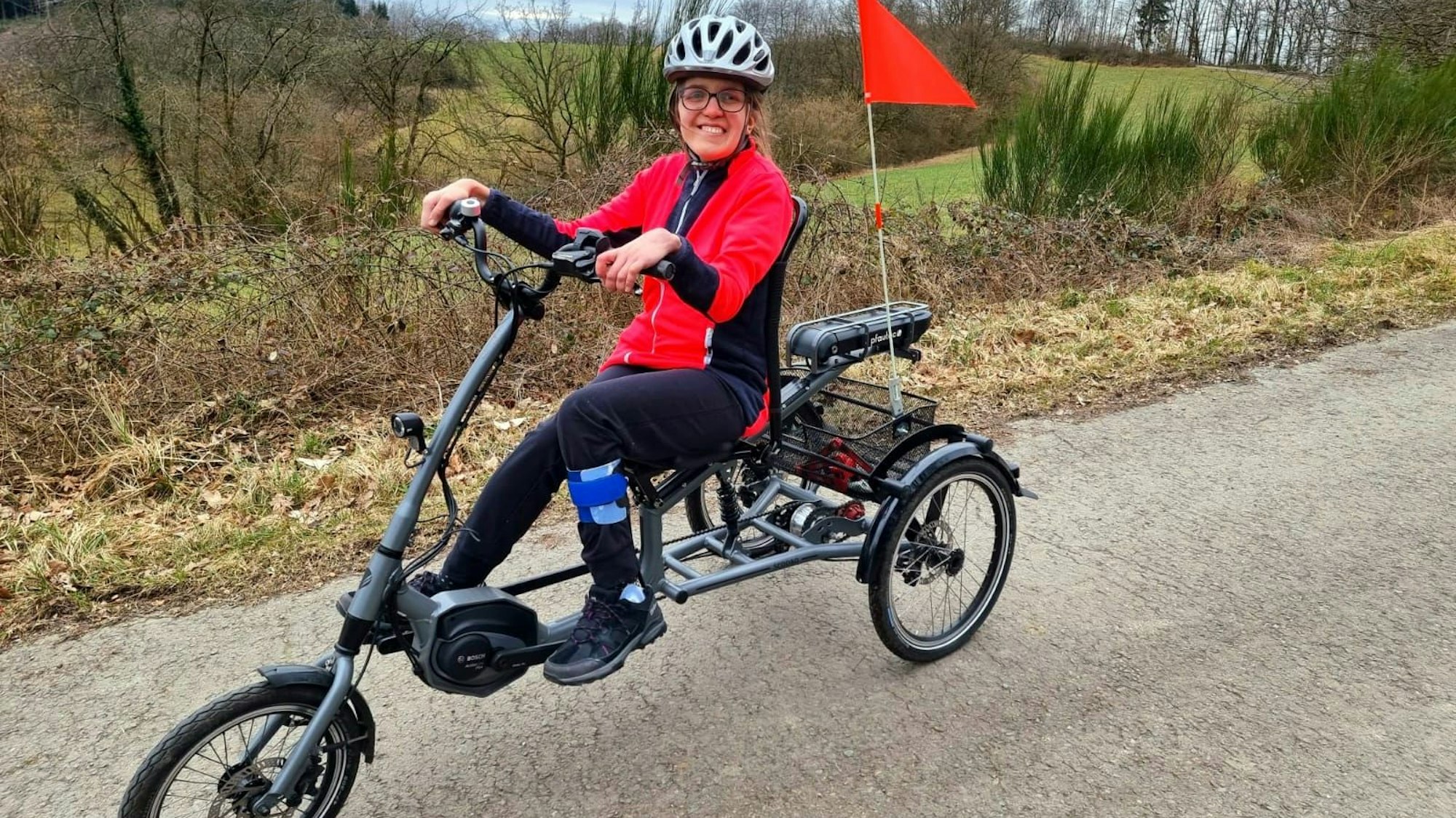 Eine Frau, die Brille und Fahrradhelm trägt, sitzt auf einem speziellen Fahrrad.