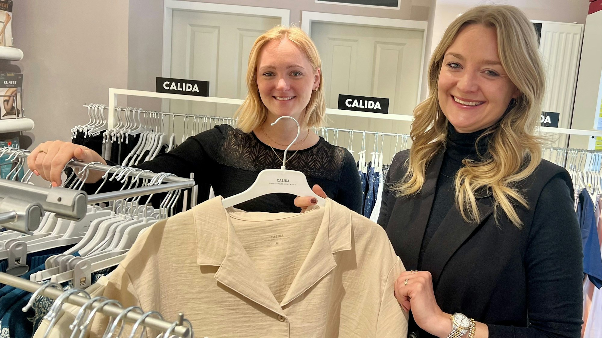 Zwei junge Frauen stehen zwischen den Kleiderstangen des Wäschegeschäfts ihrer Mutter.