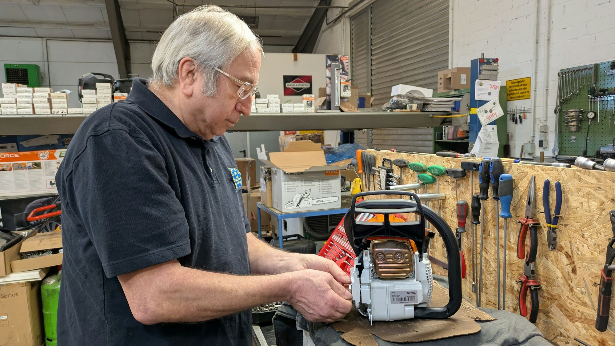 Ein Mann steht in einer Werkstatt und hantiert an einer Kettensäge.