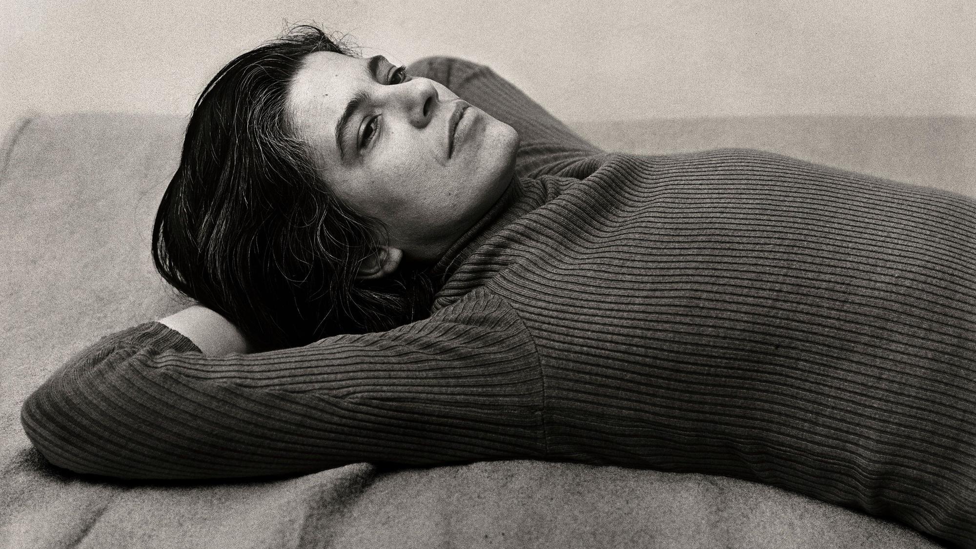 Susan Sontag hat sich in dieser Schwarz-Weiß-Fotografie auf einer Decke ausgestreckt und die Arme hinter dem Kopf verschränkt.