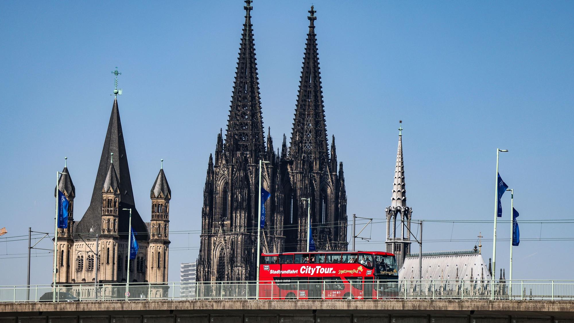 Ein City-Tour Bus fährt bei sonnigem Wetter am Dom vorbei über die Deutzer Brücke.