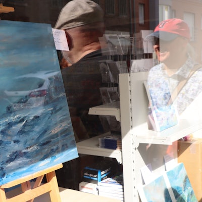 Ein Bild in einem Schaufenster, darin spiegeln sich einige Betrachter der Kunstmeile.