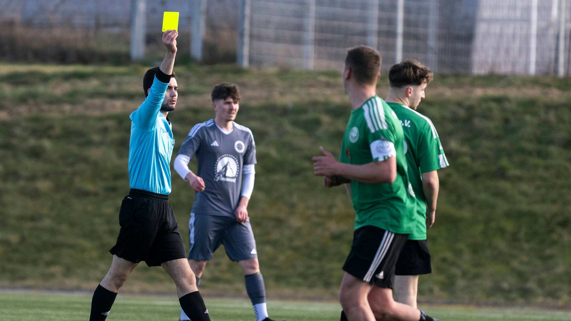 Ein Fußballer, der mit der Gelben Karte verwarnt wird, wendet sich vom Schiedsrichter ab.