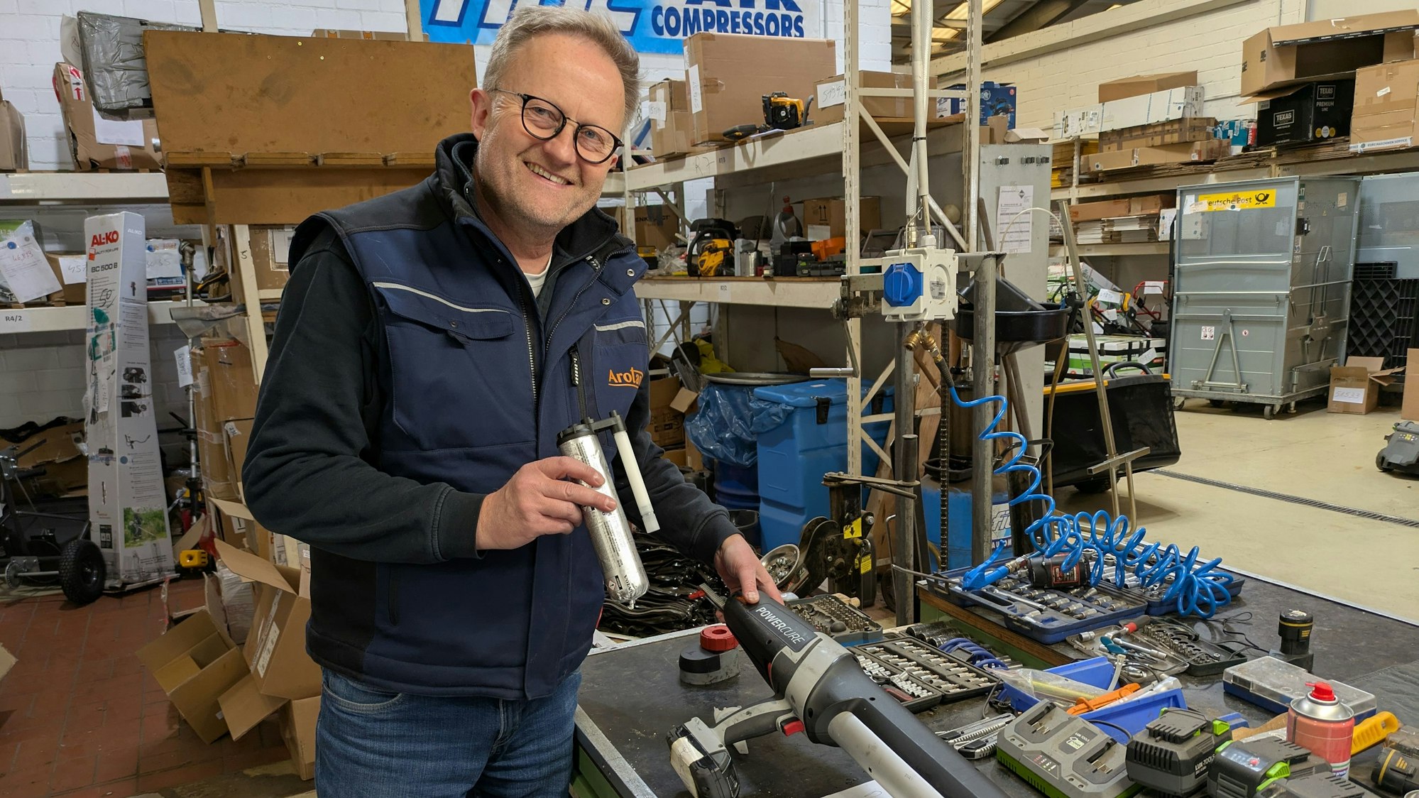 Ein Mann steht in einer Werkstatt mit einer Klebepistole.