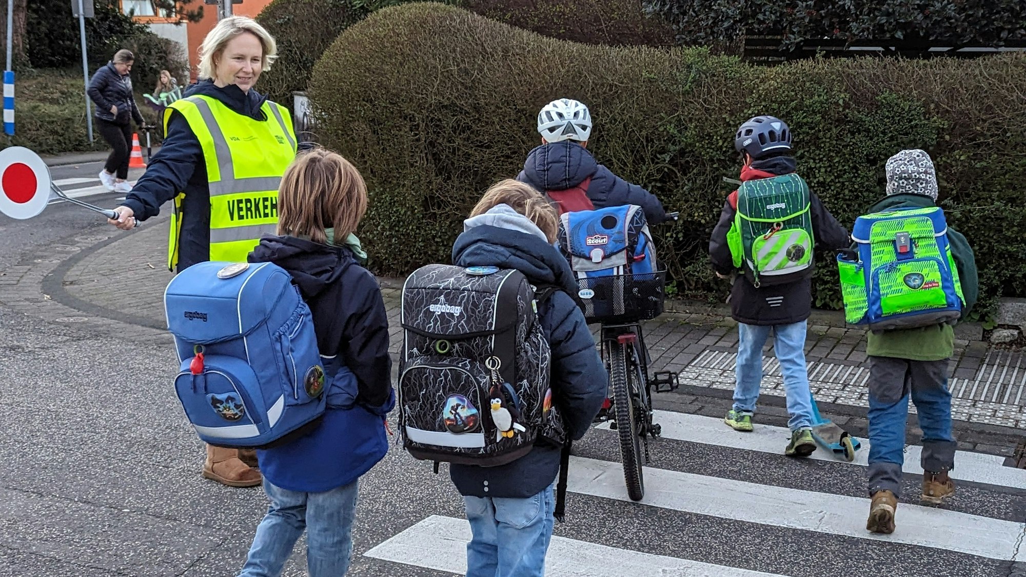 Eine Frau in Warnweste geleitet Kinder über einen Zebrastreifen.
