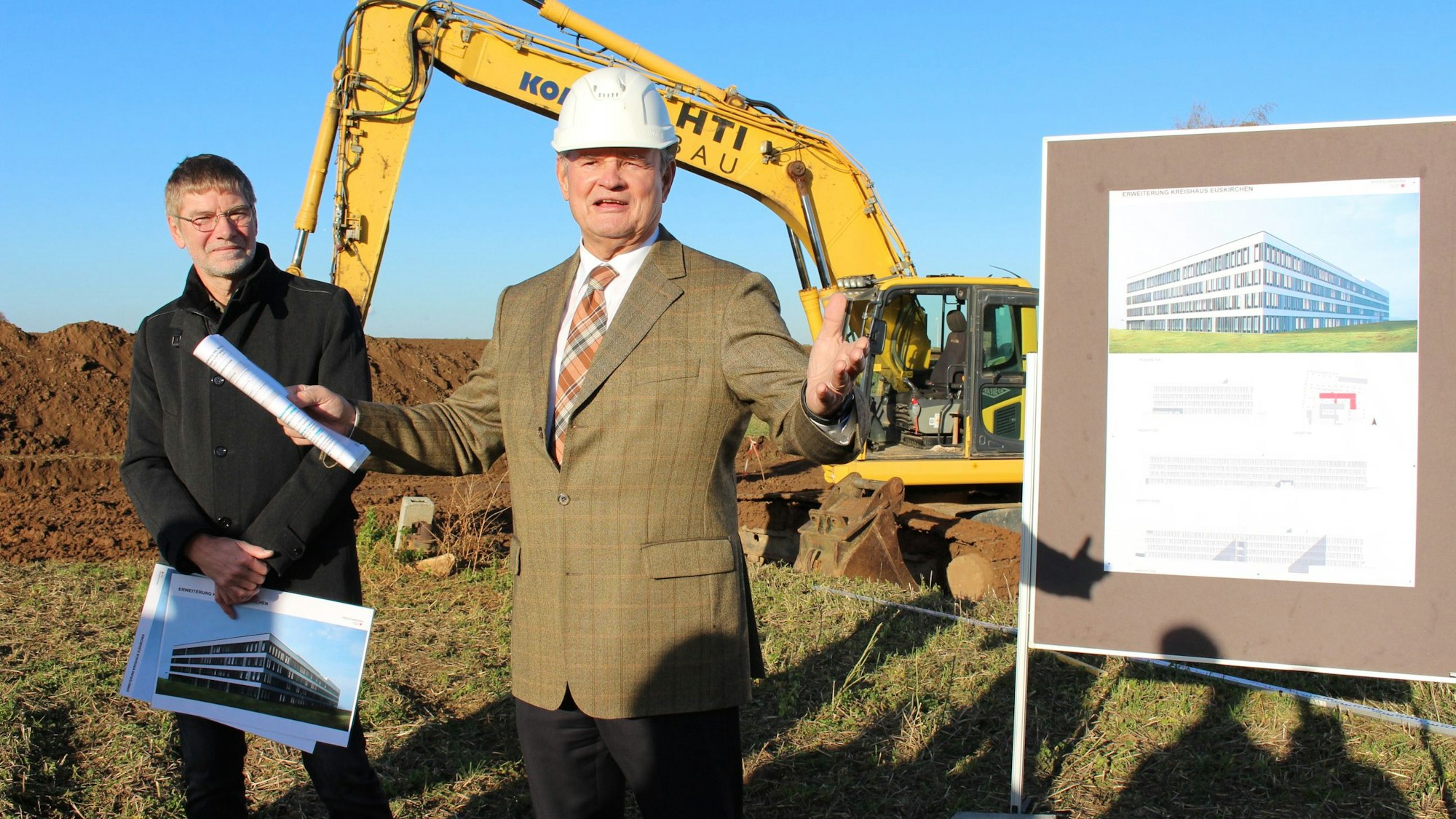 Das Archivbild zeigt den damaligen Landrat Günter Rosenke mit Bauhelm vor einem Bagger. Neben Rosenke steht ein Mann, der eine Animation des Anbaus in der Hand hält.