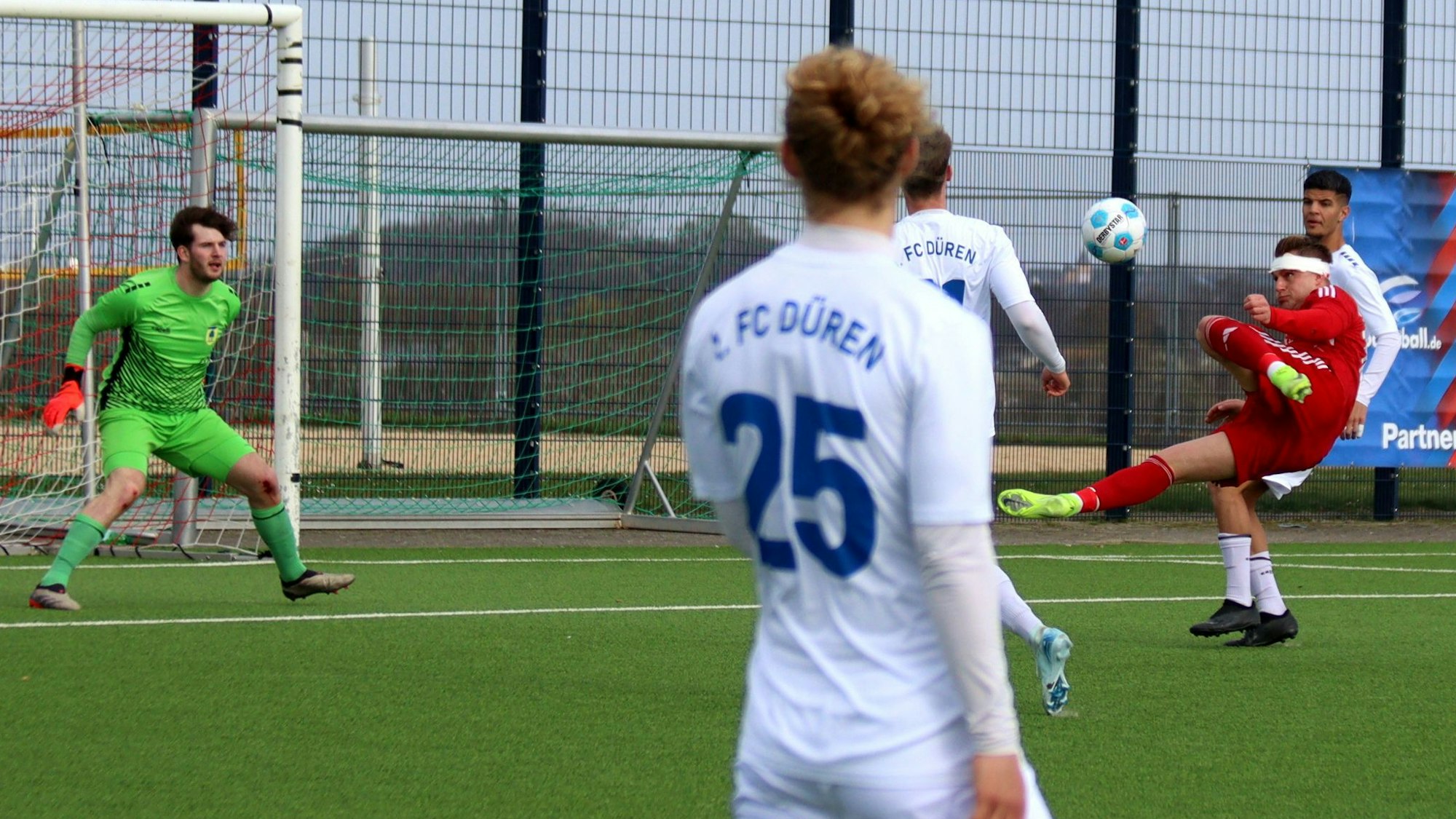 Ein Fußballspieler mit einem Kopfverband versucht einen Seitfallzieher.