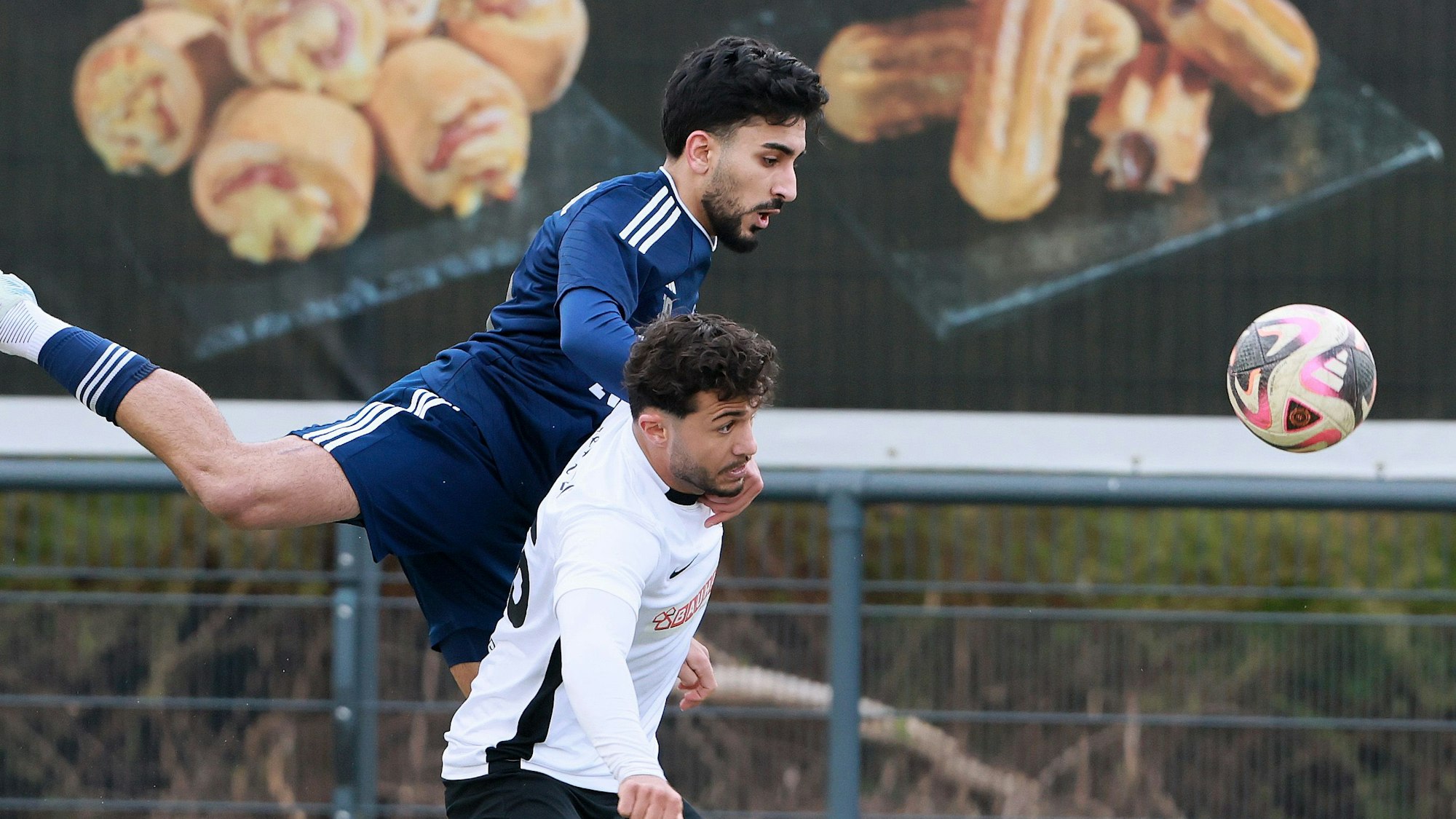 Das Foto zeigt der zwei Fußballer im Zweikampf, der in Weiß gekleidete Frechener wird vom Vichttaler in Blau übersprungen
