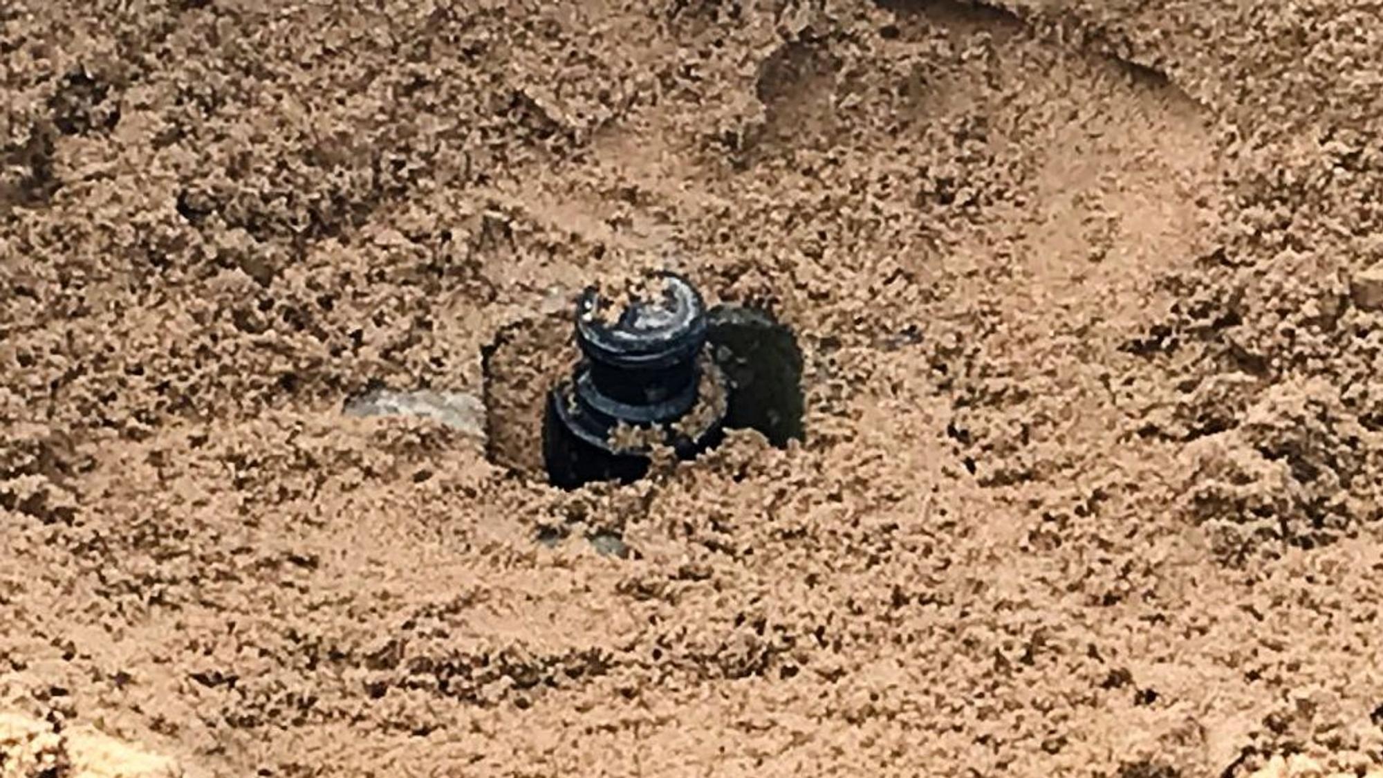 Eine Handgranate aus dem Zweiten Weltkrieg steckt in Sand. Sie wird später kontrolliert gesprengt.