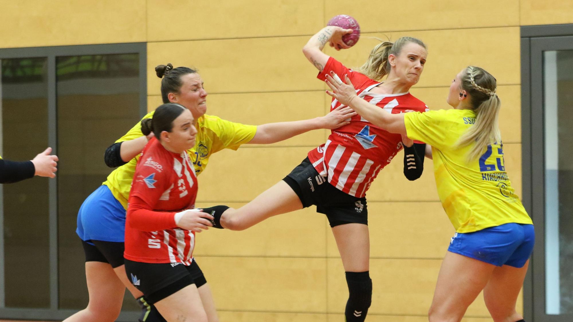 Corinna Schmitz beim Wurf. Eine Gegenspielerin blockt sie, eine andere greift nach ihrem Trikot.