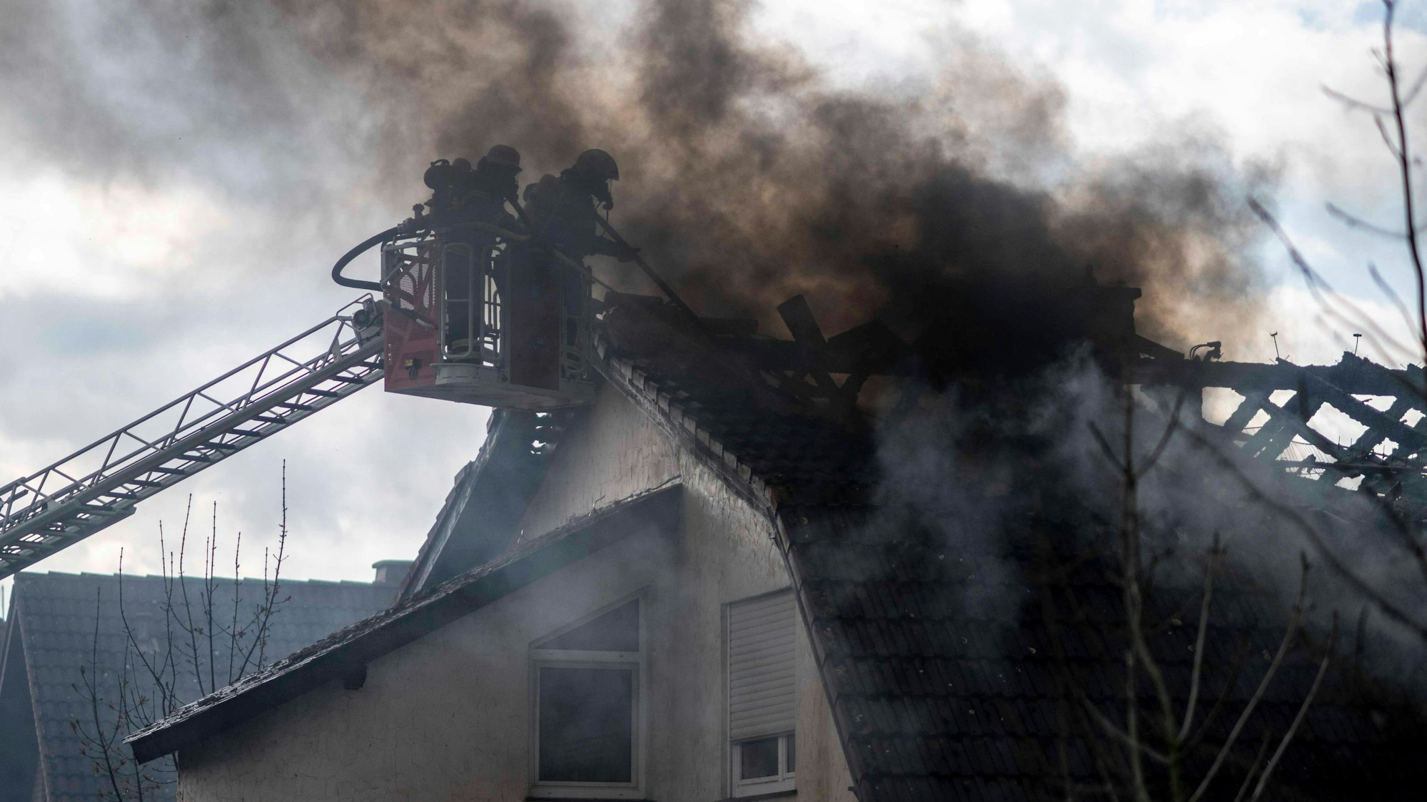 Das Bild zeigt zwei Feuerwehrleute im Korb einer Drehleiter. Sie bekämpfen im dichten Rauch einen Dachstuhlbrand.