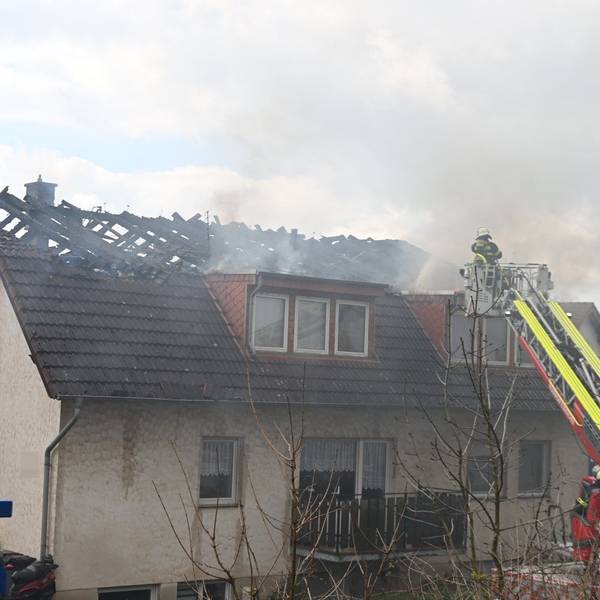 Feuerwehrleute löschen von einer Drehleiter aus den Brand im Dachstuhl eines Mehrfamilienhauses in Zülpich-Dürscheven.