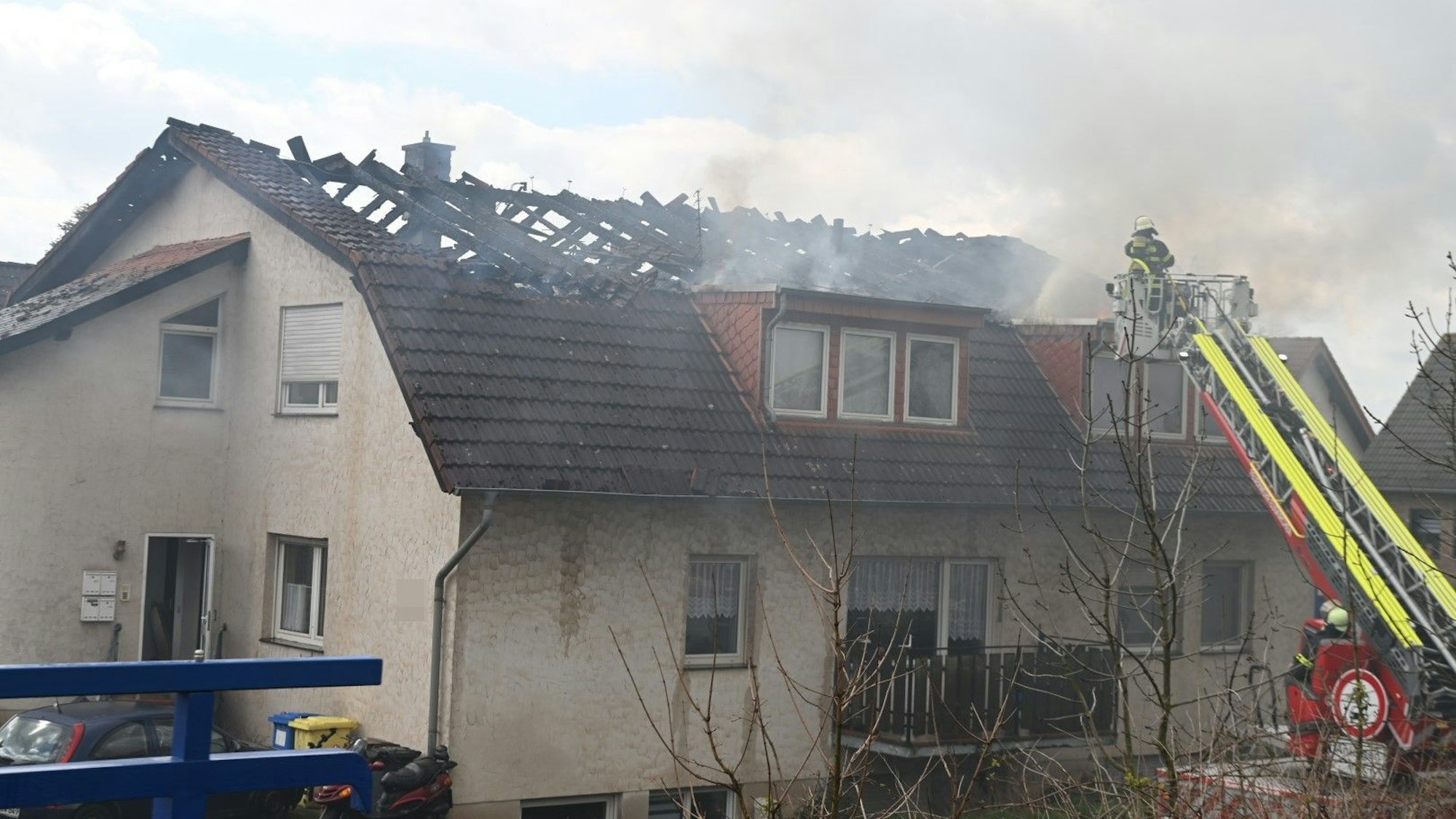 Feuerwehrleute löschen von einer Drehleiter aus den Brand im Dachstuhl eines Mehrfamilienhauses in Zülpich-Dürscheven.