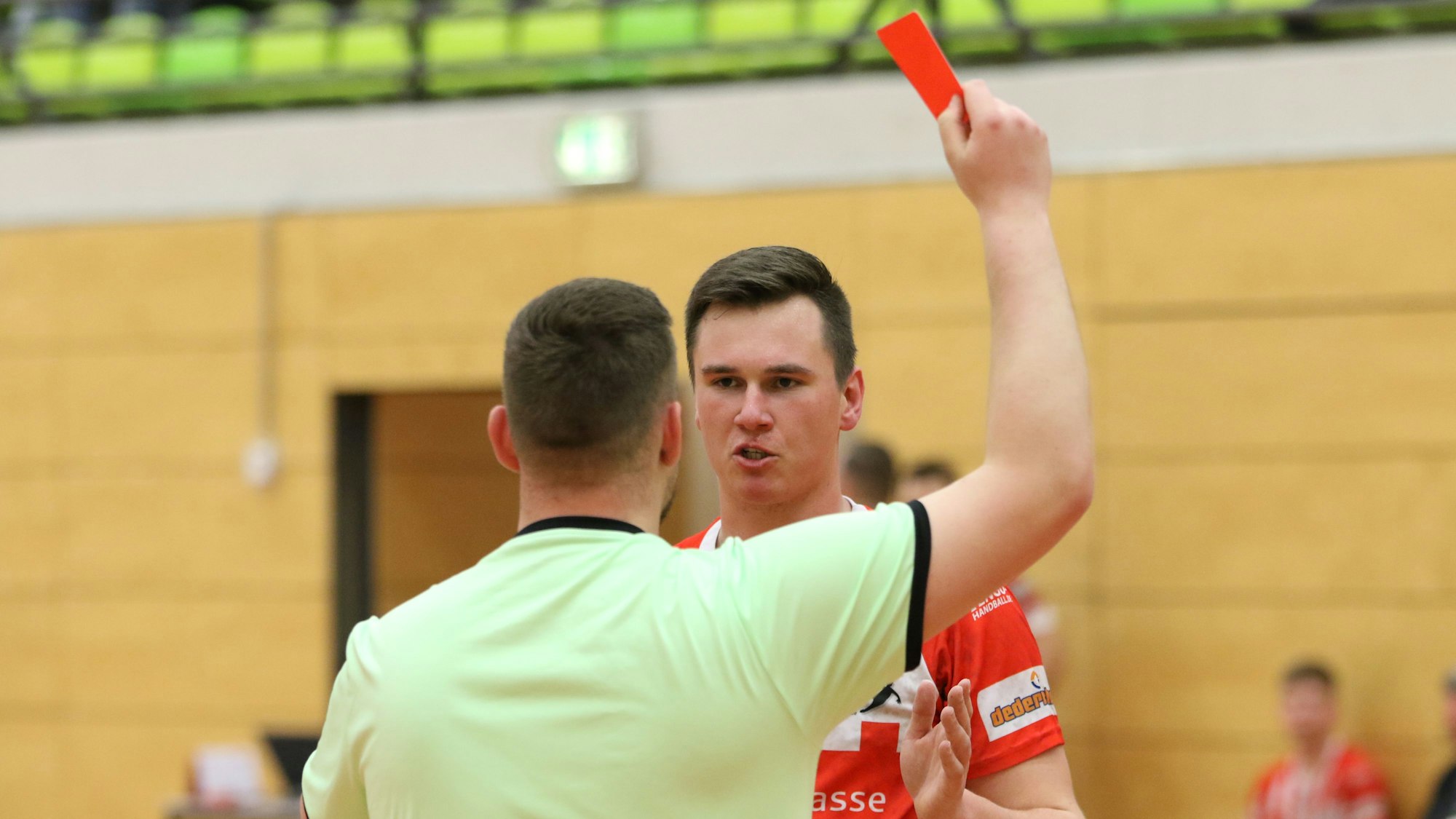 Der Schiedsrichter hält eine Rote Karte in der Hand. Der Verurteilte hat Redebedarf.