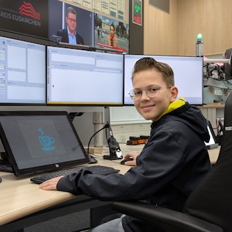Ein junger Besucher hat vor mehreren Bildschirmen und einer großen Bildschirmwand Platz genommen.
