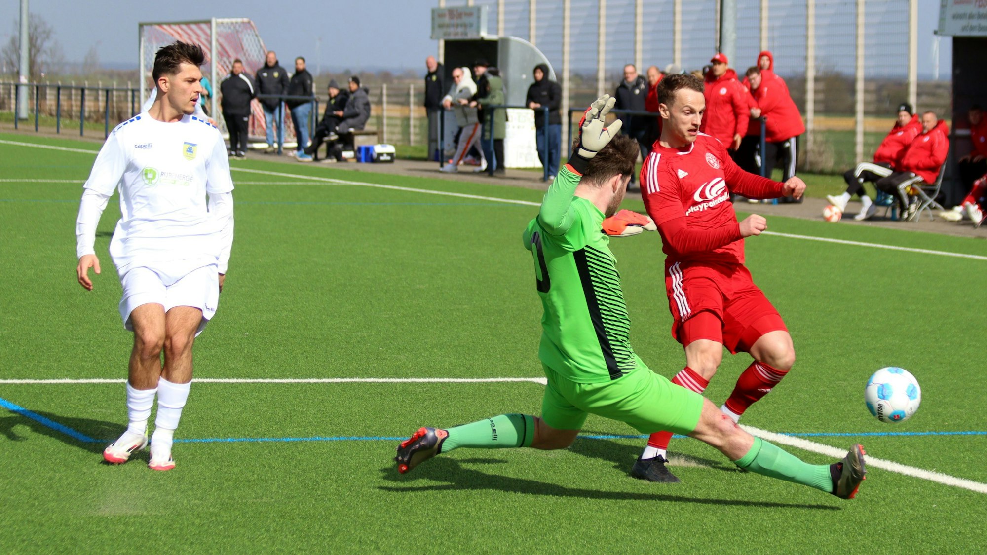 Ein Fußballer will den Ball am Torwart vorbeilegen, der sich ihm entgegenwirft.