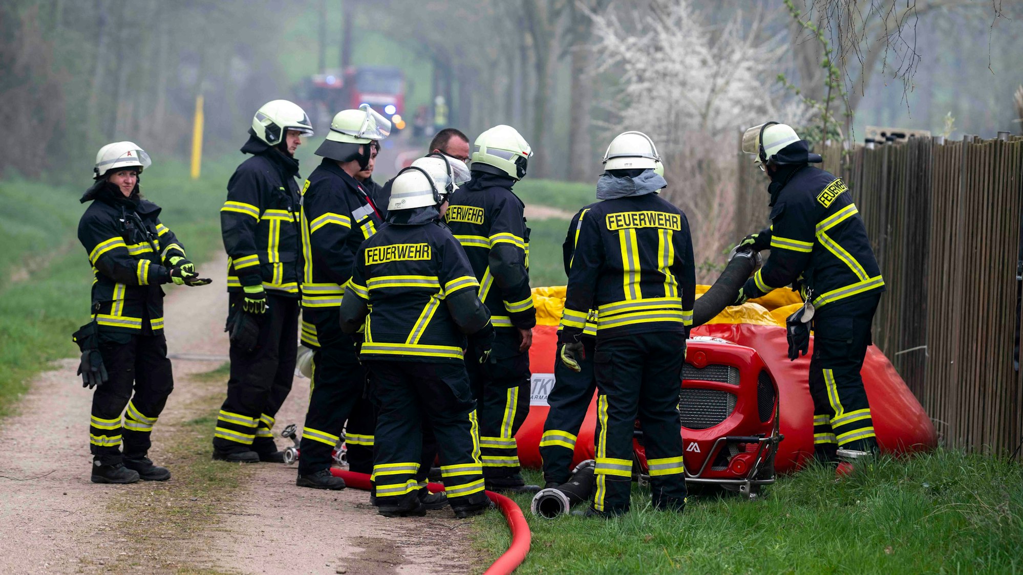 Zahlreiche Feuerwehrleute stehen an einem Faltbehälter, davor steht eine tragbare Pumpe. Sie sind Bestandteile einer Wasserversorgung, die aus einem Bach aufgebaut wird.