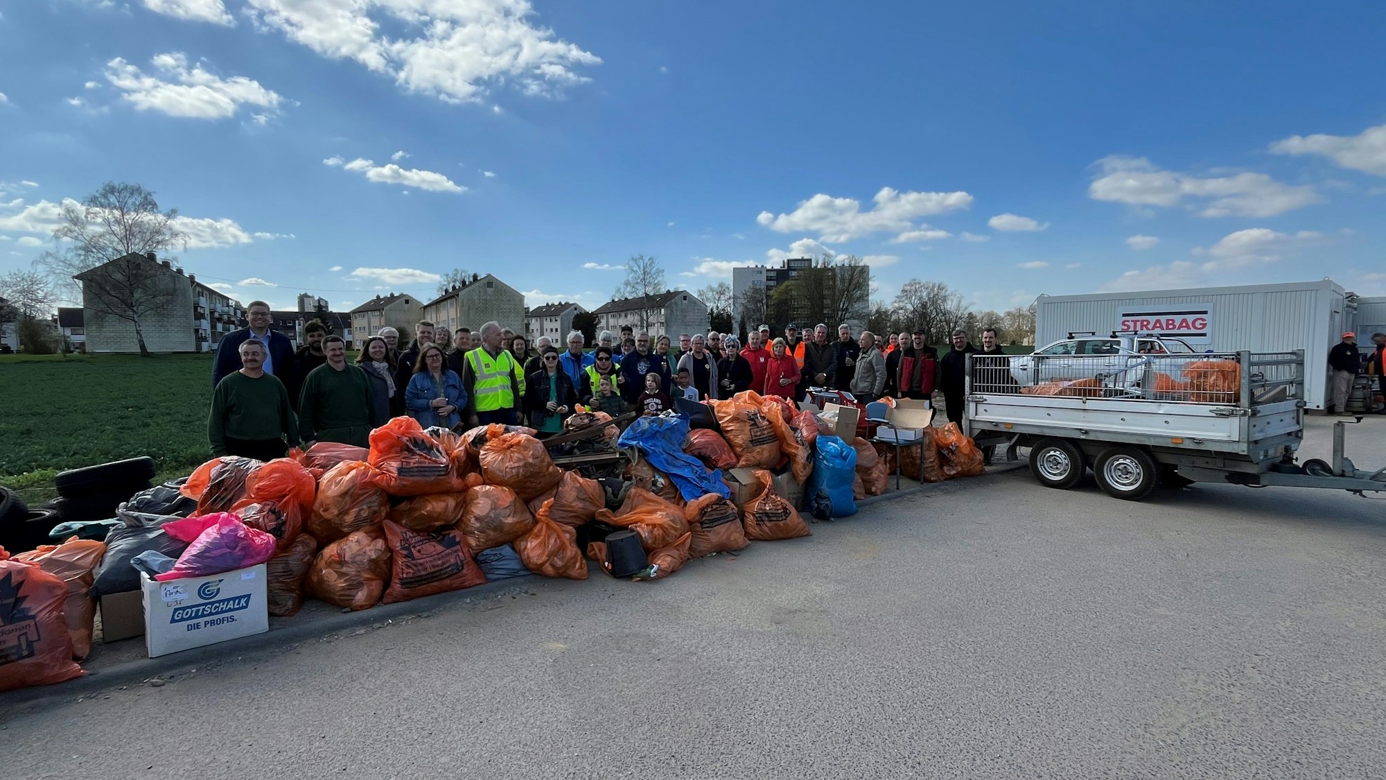 Freiwillige stehen vor zahlreichen orangen Müllsäcken.
