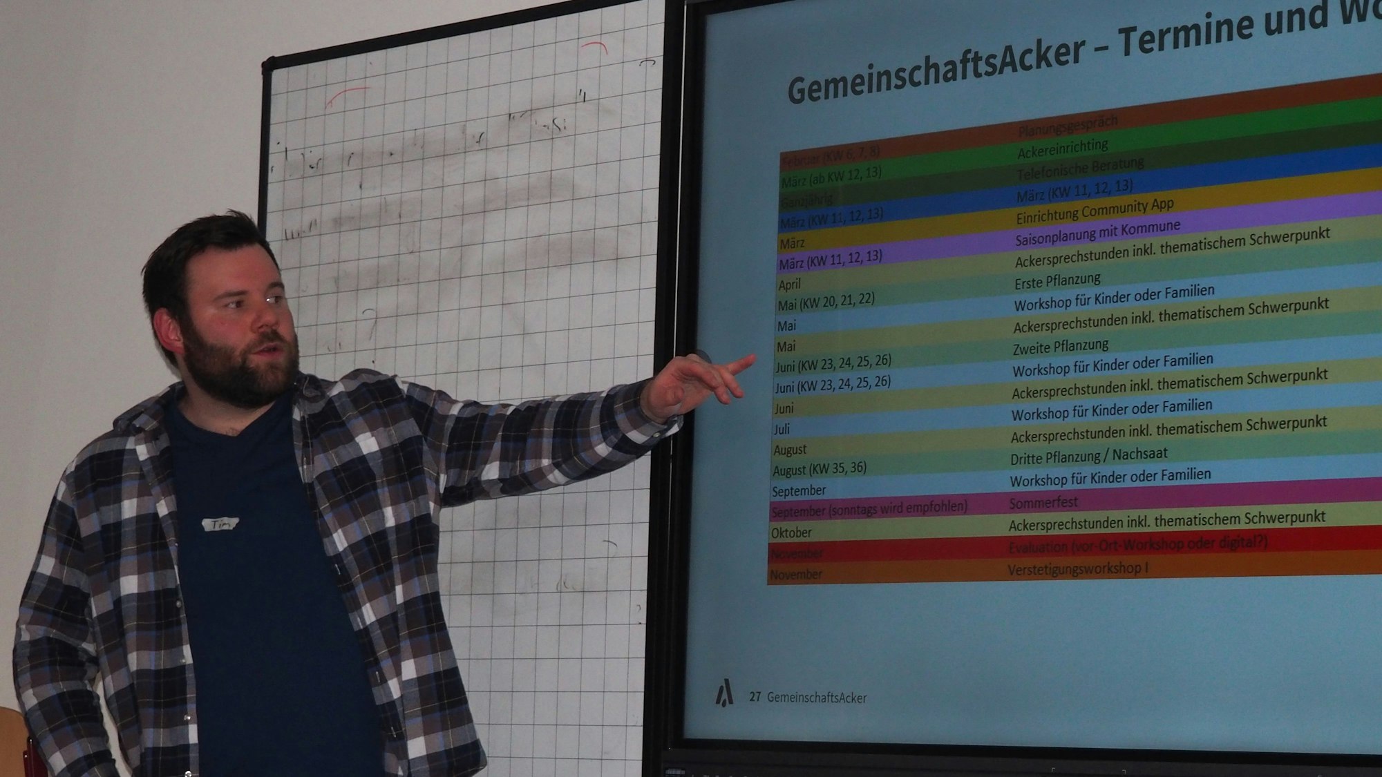 Tim Genders steht an einem Smartboard und stellt die Pläne für den Gemeindegarten vor.