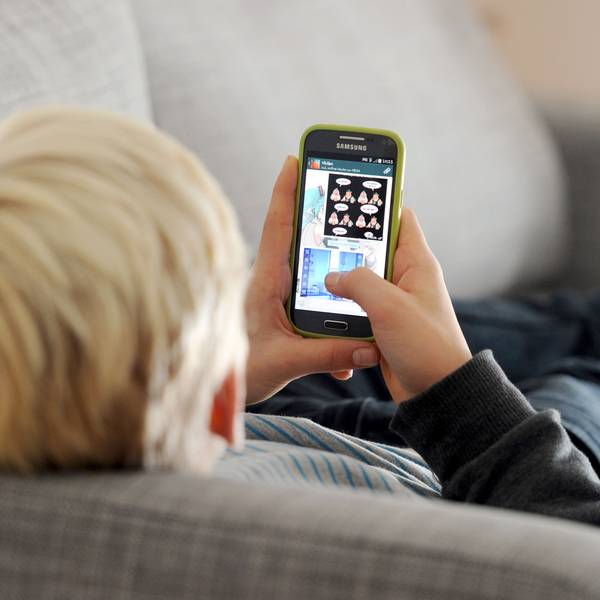 Ein Jugendlicher liegt auf einem Sofa und blickt auf sein Smartphone.