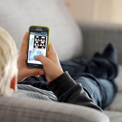 Ein Jugendlicher liegt auf einem Sofa und blickt auf sein Smartphone.