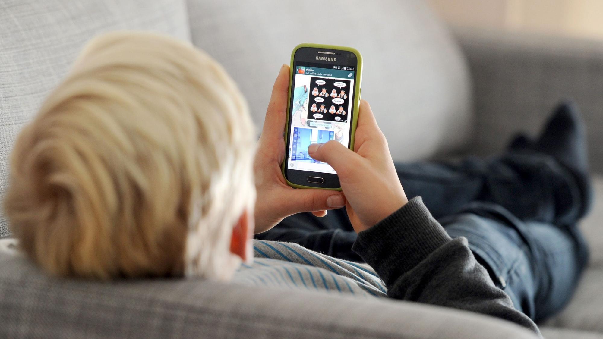 Ein Jugendlicher liegt auf einem Sofa und blickt auf sein Smartphone.