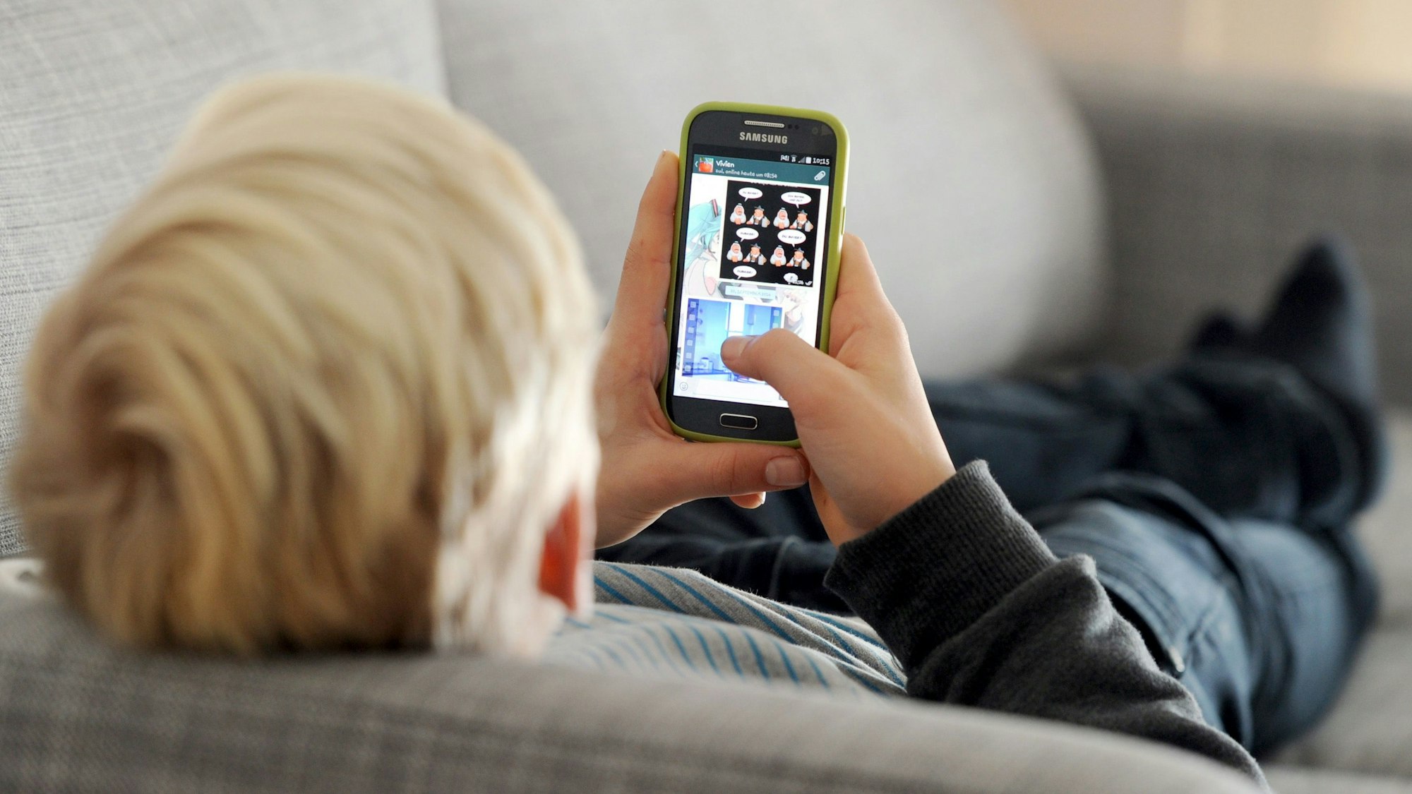 Ein Jugendlicher liegt auf einem Sofa und blickt auf sein Smartphone.