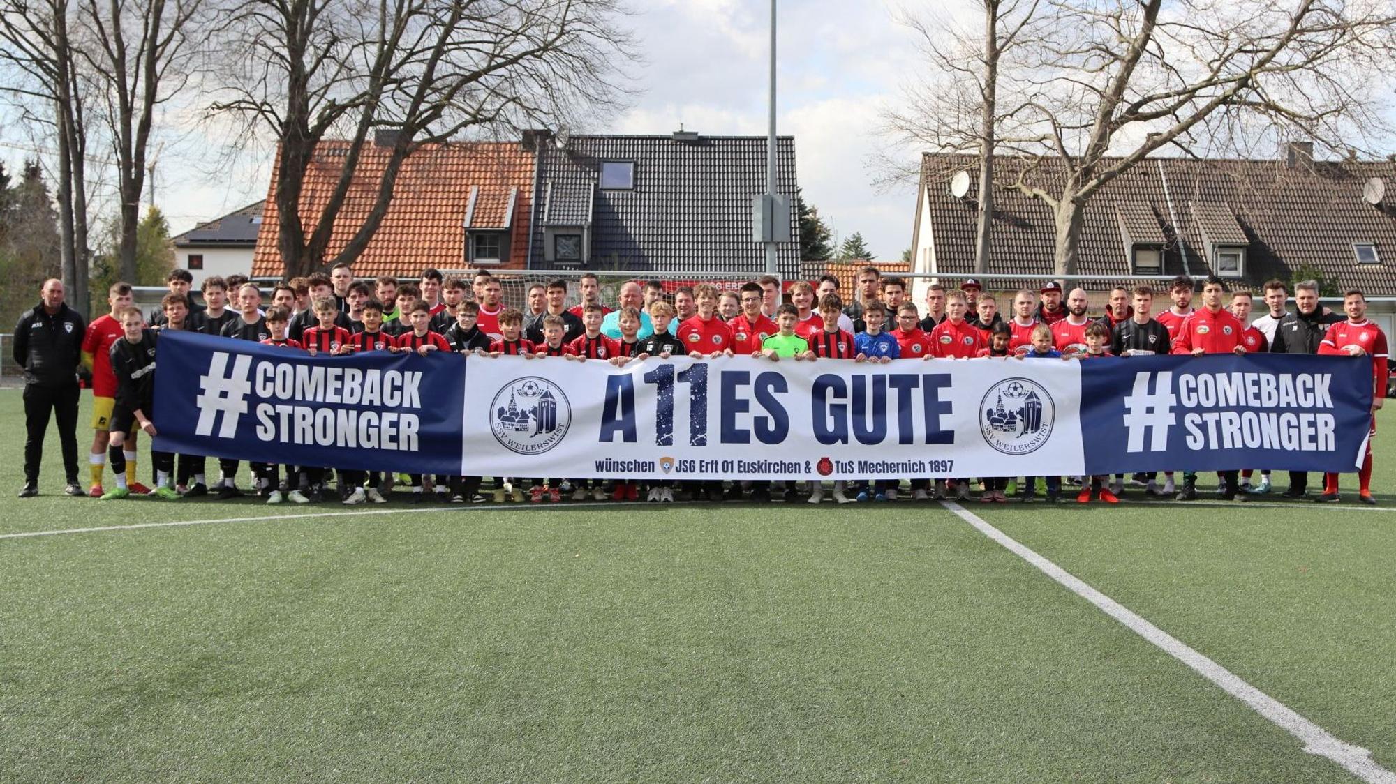 Das Bild zeigt die Mannschaften der JSG Erft Euskirchen und der TuS Mechernich, die vor dem Spiel ein Plakat hochhalten.
