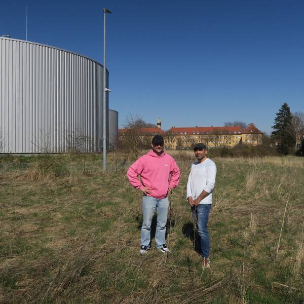 Zwei Männer stehen auf einer Wiese neben Wasserspeichern.