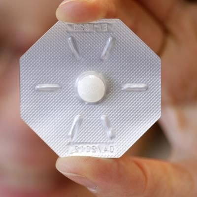 Eine Frau hält ein Tabletten-Blister mit der „Pille danach“ vor ihr Auge.